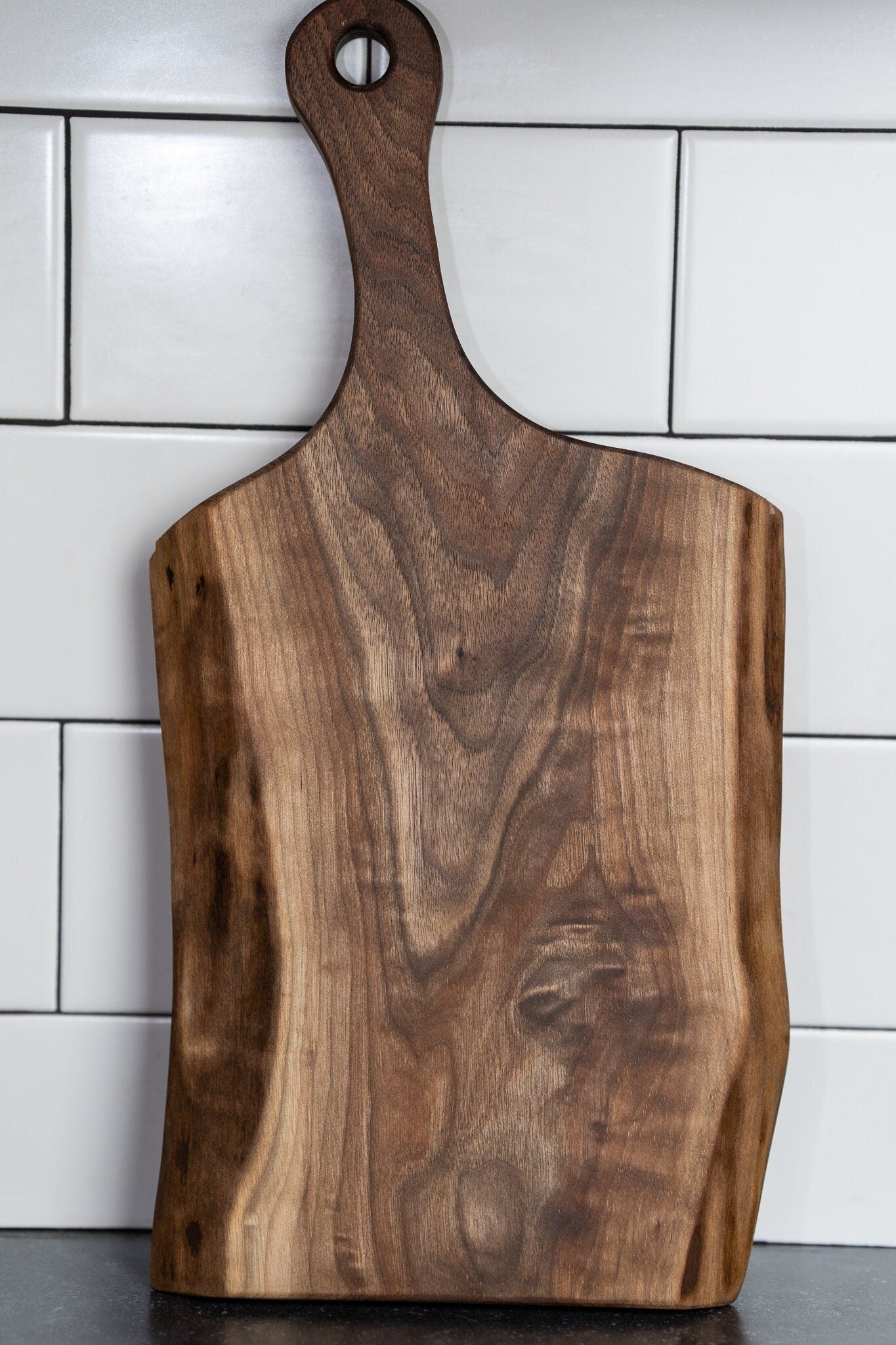 This image shows a handcrafted live edge black walnut charcuterie board with a handle. The board features rich wood grain, natural edges, and a polished finish. It’s great for serving or display and makes a beautiful, functional add to any kitchen.