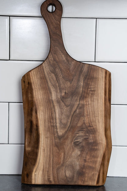 This image shows a handcrafted live edge black walnut charcuterie board with a handle. The board features rich wood grain, natural edges, and a polished finish. It’s great for serving or display and makes a beautiful, functional add to any kitchen.